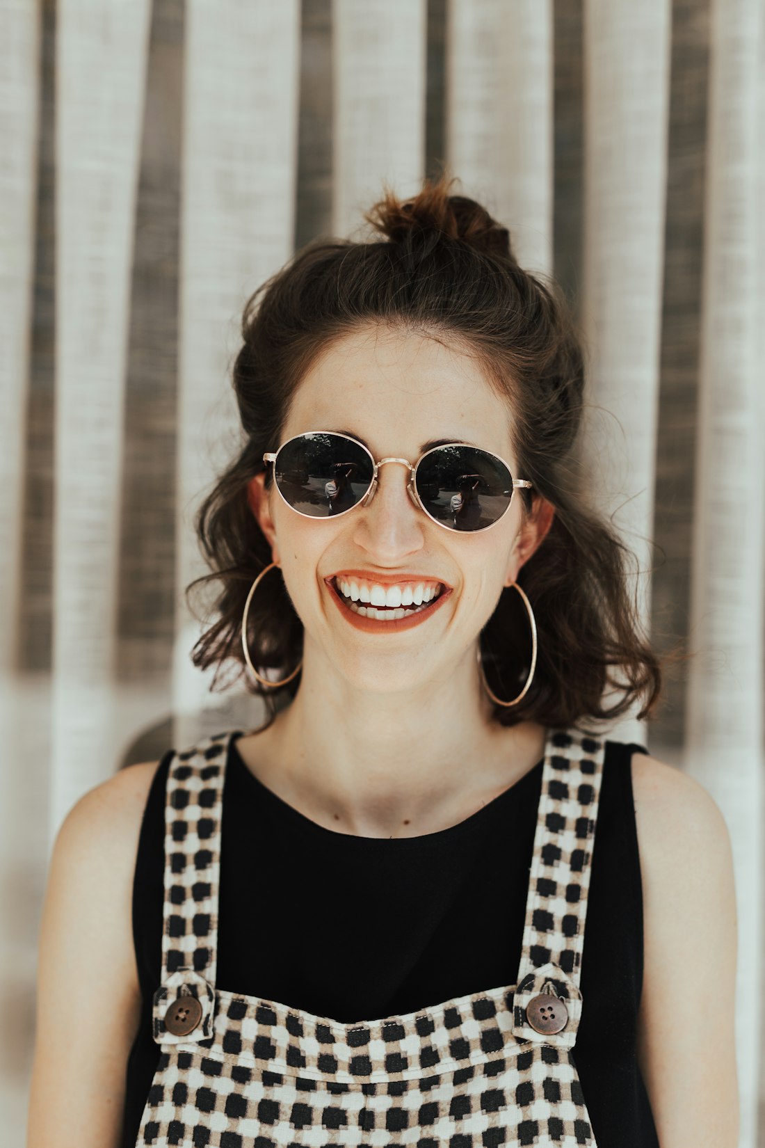 Lachende Frau mit Sonnenbrille vor gestreiftem Hintergrund